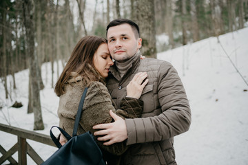 Stylish man with his cute young wife embrace in the forest on the wooden bridge. Romantic moment.