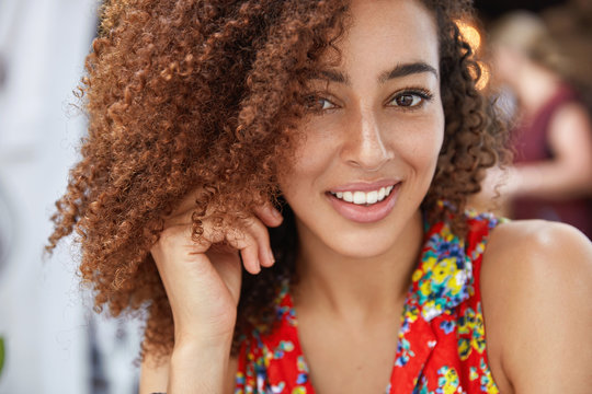 Close up shot of pleasant looking cheerful African American female with joyful expression, dressed in bright summer clothing, happy to spend leisure time with close person. People, ethnicity
