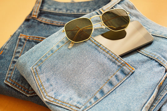 Picture of two jeans with mobile in pocket and glasses on craft wooden background