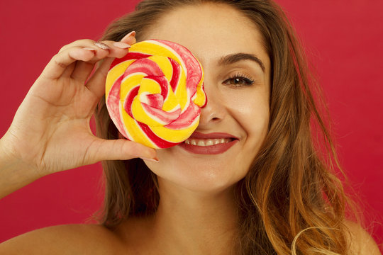 Portrait of a happy pretty girl holding sweet candy over red background