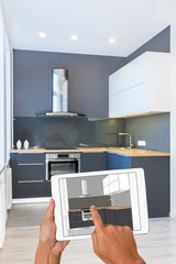 Business hands holding tablet with modern kitchen interior sketch. In the background real finished kitchen interior design. Kitchen presentation. Home Interior Design Software Programs. Computer.