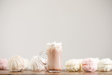 Cocoa in a glass mug and a gentle fresh meringue on a wooden background.