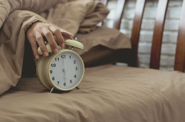 alarm clock with lazy woman hand put on for stop alarm clock to snooze from wake up on bed in...