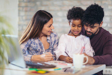 Mom and dad drawing with their daughter. Girl and mixed race parents having fun at home.