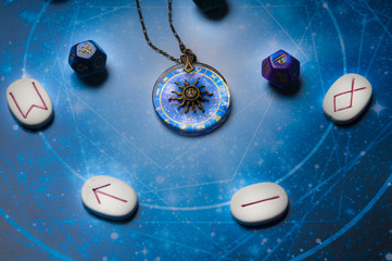astrology dice, zodiac symbols on pendant, runes stones over blue horoscope 