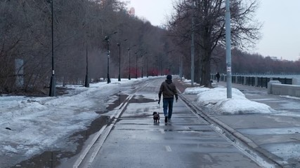 Man walks with a dachshund in the park at the river