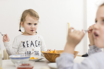 Little Kid Looking Annoyed at Her Sister While Eating - obrazy, fototapety, plakaty
