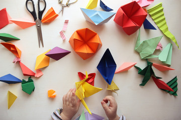 the child makes origami. Multicolored Origami and paper on  a white table. origami lesson - obrazy, fototapety, plakaty