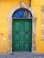 Fototapeta na wymiar old double green door in a stone frame in a yellow painted wall typical of the style of old buildings in cyprus