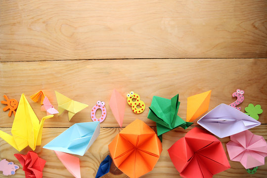 Man doing origami. Multicolored Origami and paper on  a wooden table.
lesson of origami