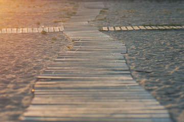 Fototapeta premium Wooden path on the beach in the rays of the setting sun.