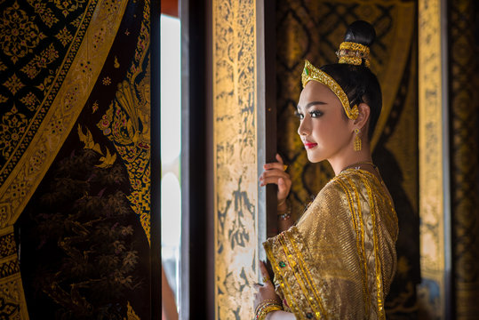 Beautiful asia woman in gorgeous antique thai dress stand near ancient gold threads old thai pattern windows in temple of  Thailand.