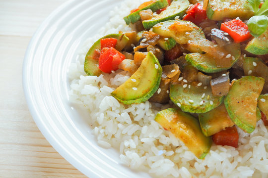 Rice with vegetables (zucchini, eggplant, onion, pepper) on wooden background. Asian cuisine.
