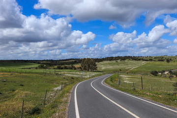 Road with green grass field under white clouds and blue sky. Country side landscape in Portugal