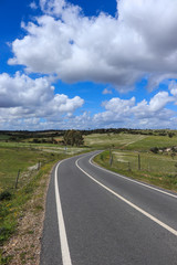 Fototapeta na wymiar Road with green grass field under white clouds and blue sky. Country side landscape in Portugal