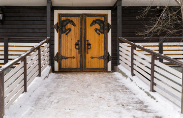 Original design, wooden doors with metal horses. Entrance to the stable in winter	