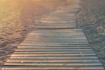 Wooden path on the beach in the rays of the setting sun.