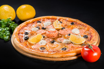 Delicious juicy pizza with salmon, lemon and olives on wooden board on dark background