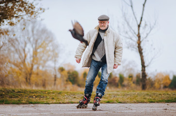 An elderly original man has fun skating on roller skates. The man is spreading hands. People and...