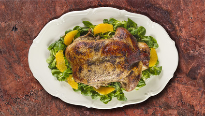 Baked duck in oranges and field salad or lamb's lettuce  on white plate on granite counter top.