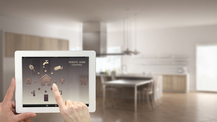 Smart remote home control system on a digital tablet. Device with app icons. Blurry interior of minimalist kitchen in the background, architecture design