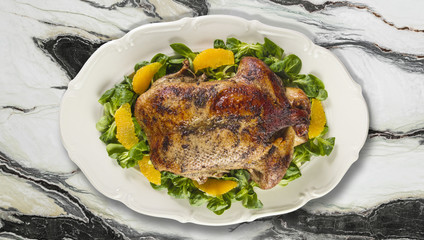 Baked duck in oranges and field salad or lamb's lettuce  on white plate on granite counter top.