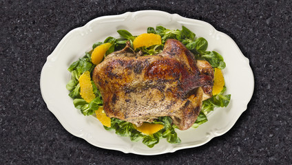 Baked duck in oranges and field salad or lamb's lettuce  on white plate on granite counter top.