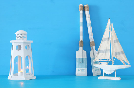 nautical concept with white decorative lighthouse lantern, wooden oars and boat over blue background.