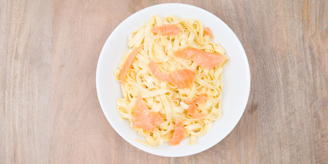 fresh pasta with salmon in a white plate at top view