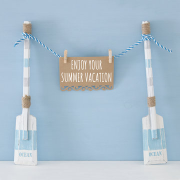 nautical concept with wooden decorative boat oars and note hanging on a string over blue background.