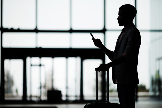 Silhouette of businessman profile texting in smartphone while waiting for departure in airport lounge