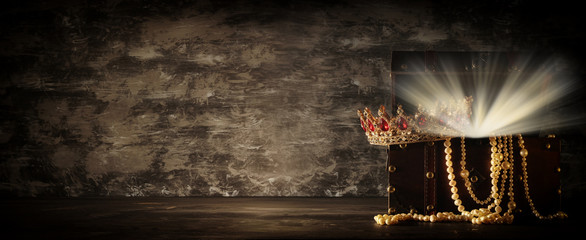 Image of mysterious opened old wooden treasure chest with light and queen/king crown with red...