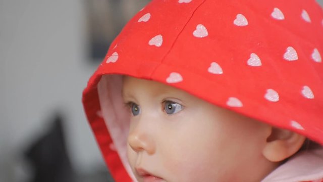 Close-up shot of blue eyed baby face watching cartoons. The child in red hood with silver hearts pattern looking with interest what happening on the screen