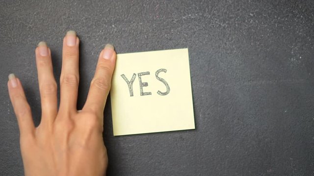 Closeup woman's hand sticking note with Yes word on the blackboard - video in slow motion