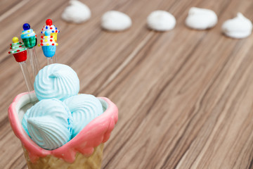 blue meringue in the pink cone with cupcakes on wood background and white meringues