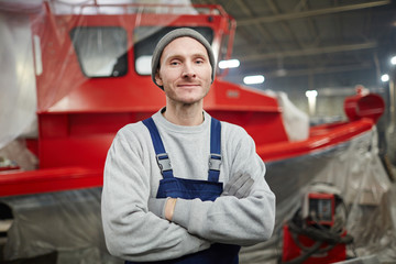 Young cross-armed engineer in workwear on background of new model of boat that he invented