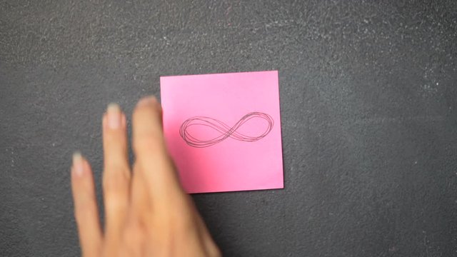 Closeup woman's hand sticking note with Infinity sign on the blackboard - video in slow motion