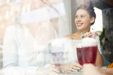 One of two girls looking at her friend during talk in cafe by drink in the middle of the day