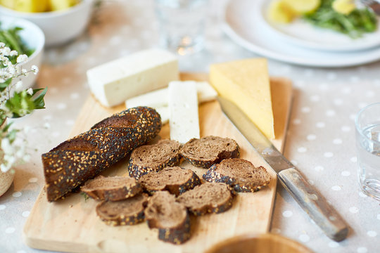 Several slices of fresh rye bread and cheese on wooden board among other food on served festive table