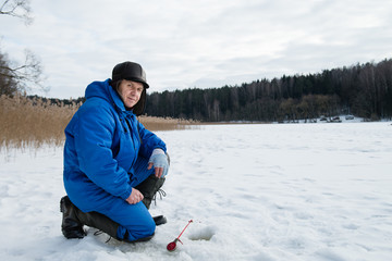 Fototapeta na wymiar Old man fishing on a lake at cold winter day