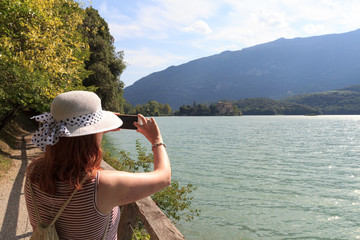 Tourist woman taking picture of Castle Castel Toblino with smartphone in Italy