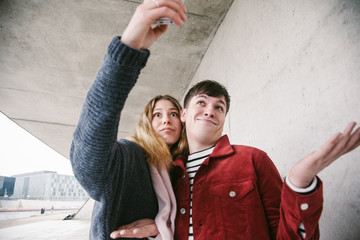 Young Cute Couple having fun while taking weird Seflies with their Smartphones in Berlin