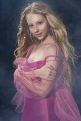 Beautiful curly blonde teenager child girl wearing a pink air dress made of veil swith hair flying...