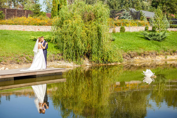 newlyweds hugging while standing on wooden pier near lake at sunny summer day