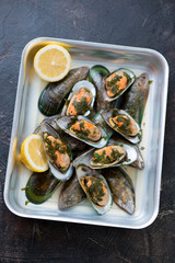 Baking tray with kiwi mussels stewed in white wine, brown stone surface, vertical shot