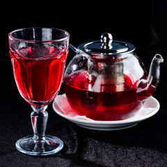 Glass teapot with hot red tea and high glass on dark background