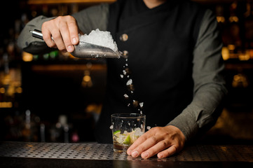 Barman adding ice into the glass with a cane sugar and lime