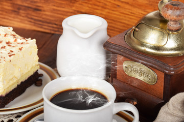 old coffee grinder, cake with cream and coffee in a beige cup with a jug full of milk