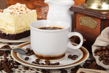 black hot coffee with vanilla chocolate cake next to a coffee grinder