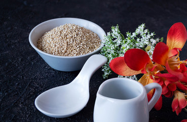 Casserole with empty porcelain quinoa, spoon and jugs and white, orange and yellow flowers.
